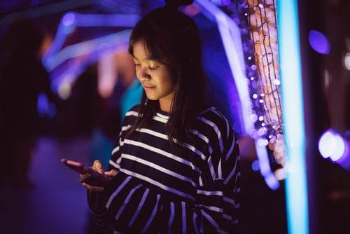 Asian young girl using a mobile phone in downtown, Bokeh city light in background